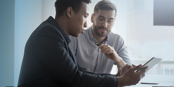 An Asian man and a white man with glasses and a beard, collaborate with a tablet An Asian man and a white man with glasses and a beard, collaborate with a tablet
